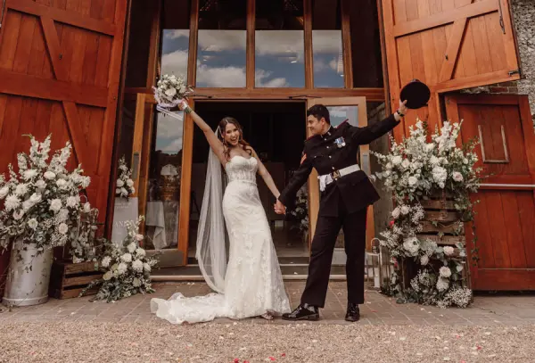 A joyful couple celebrates at an elegant barn entrance adorned with lush floral arrangements, perfect for a romantic wedding.