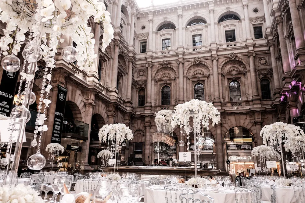 Elegant wedding venue featuring an ornate architecture backdrop, adorned with tall floral centerpieces and a spacious dining area.