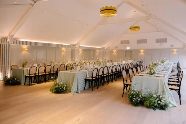 Stylish reception area featuring long tables adorned with fresh florals, elegant greenery, and warm lighting under a high ceiling.