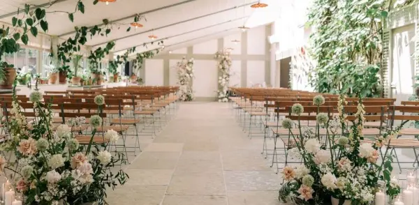 Ceremony space featuring elegant wooden seating surrounded by lush greenery and floral arrangements, creating a romantic atmosphere.