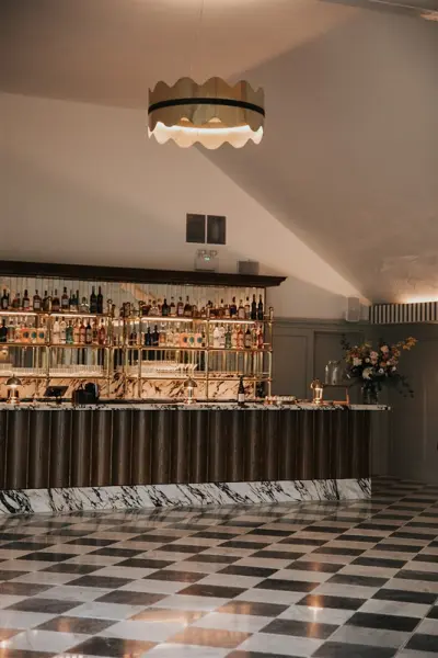 Stylish wedding bar featuring a stunning marble countertop, an extensive drink selection, and chic lighting above a checkered floor.