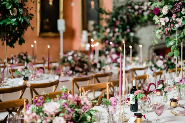 Elegant reception with beautifully set tables adorned with lush pink flowers, glowing candlelight, and rustic wooden chairs.