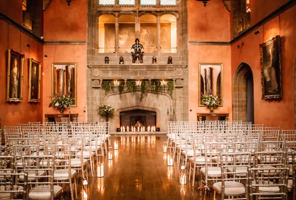 Elegant ceremony space featuring rows of chiavari chairs, a grand fireplace, and rich, warm walls adorned with artwork.