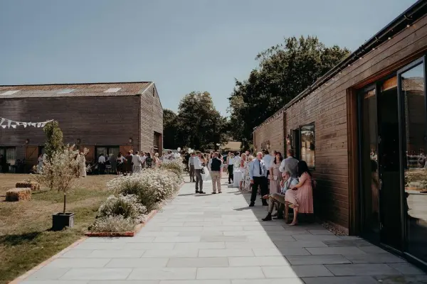 Charming outdoor space with guests mingling along a stone pathway flanked by rustic wooden buildings and lush greenery. Perfect for celebrations.