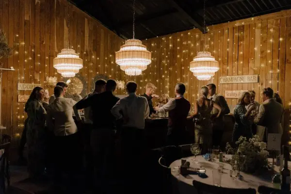 Warm, intimate venue with a wooden wall, sparkling lights, and vintage chandeliers, perfect for a cozy wedding reception atmosphere.