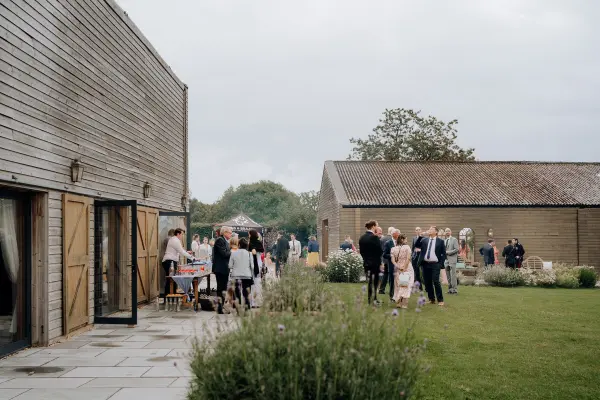 Guests mingle in a charming outdoor space, surrounded by rustic barns and lush greenery, perfect for a relaxed wedding celebration.
