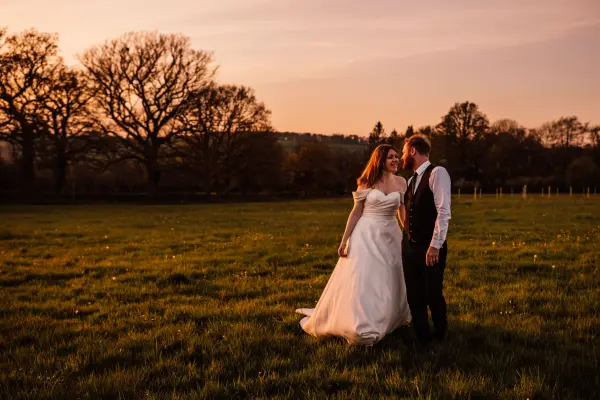 Intimate outdoor wedding in a lush green field at sunset, featuring a couple sharing a romantic moment surrounded by trees.