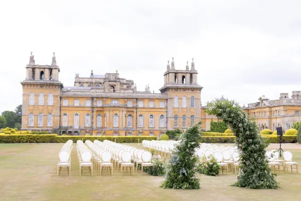 Outdoor ceremony space featuring elegant seating, lush greenery, and a grand historic building in the background, perfect for weddings.