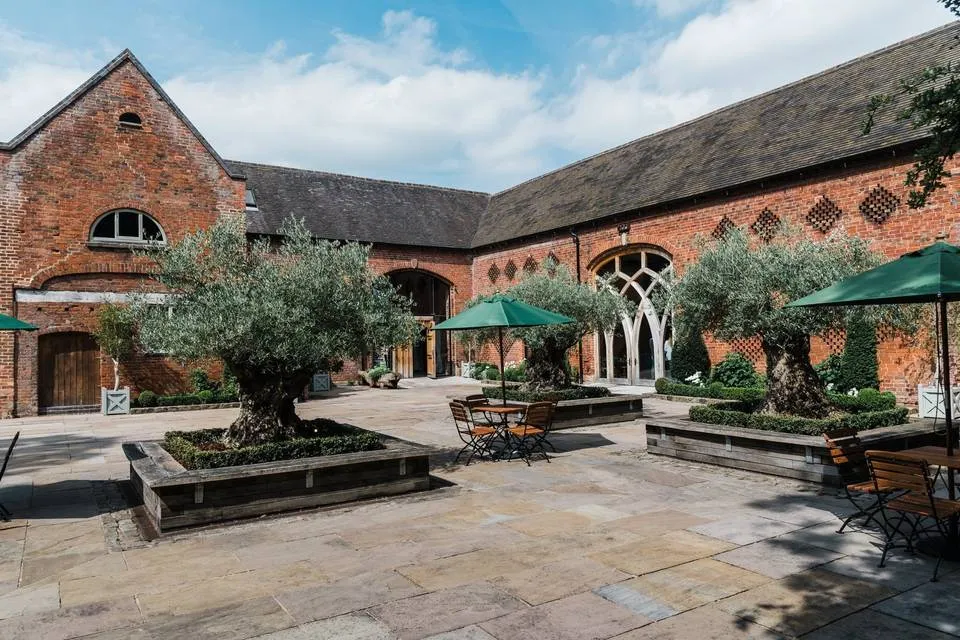 Charming outdoor courtyard featuring olive trees, stone flooring, and rustic red brick buildings, perfect for intimate wedding ceremonies.