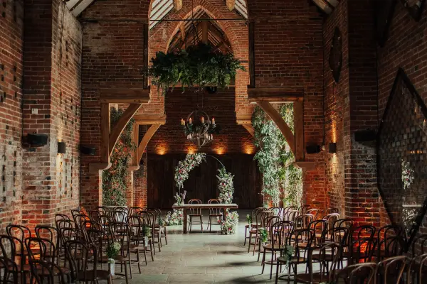 Rustic ceremony space with exposed brick walls, wooden beams, and elegant floral arrangements framing a charming altar. Cozy, intimate atmosphere.