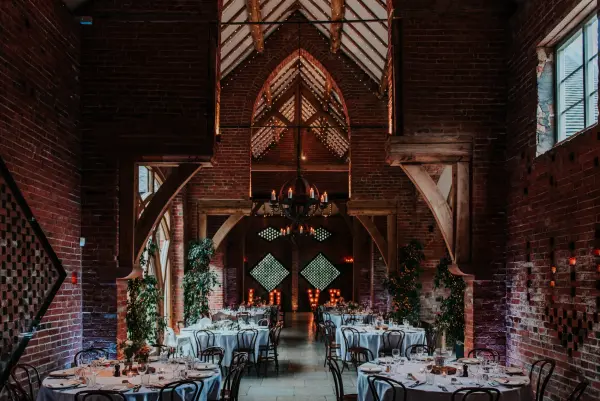 Elegant reception space featuring rustic brick walls, wooden beams, and candlelit tables adorned with greenery for a romantic atmosphere.