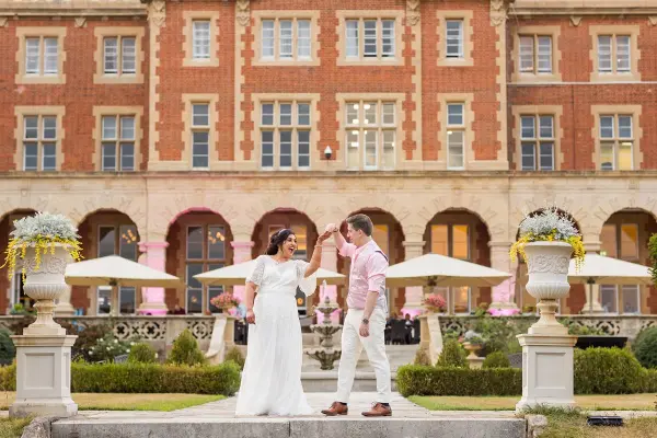 Couple dances joyfully in front of a grand brick building with elegant gardens and outdoor seating, perfect for romantic celebrations.
