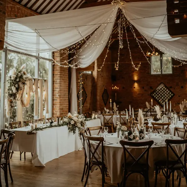 Charming reception space with elegant draping, fairy lights, rustic wooden tables, and lush floral arrangements for a romantic wedding.