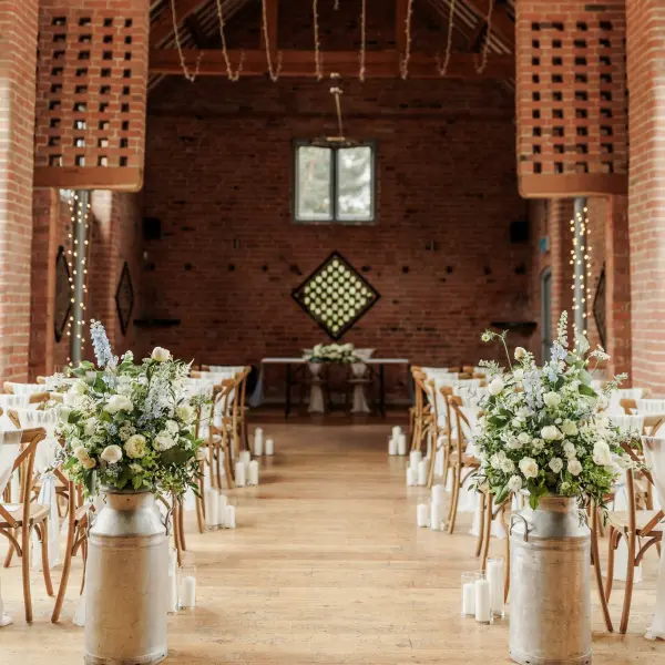 Rustic barn wedding venue featuring wooden chairs, elegant floral arrangements, and a charming brick backdrop for an intimate ceremony.