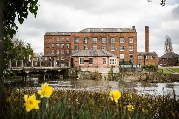 Historic red-brick wedding venue beside a tranquil river, featuring lush foreground flowers and scenic outdoor spaces for ceremonies.