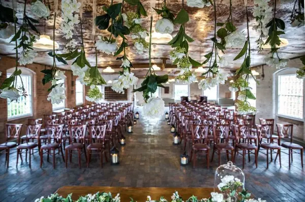 Charming indoor ceremony space featuring wooden chairs, floral garlands, and warm lighting, creating an inviting atmosphere for weddings.