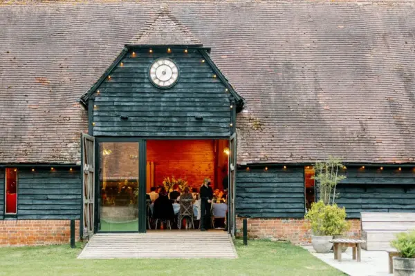 Charming rustic barn with large doors open to a lively reception, surrounded by greenery and warm string lights illuminating the space.
