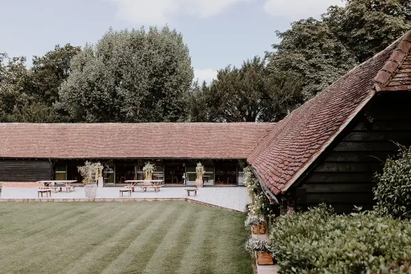 Charming rustic venue with lush green lawns, elegant outdoor seating, and a scenic backdrop of trees and a quaint barn.