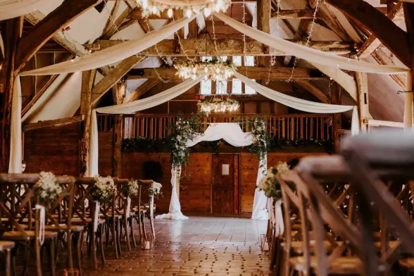 Charming rustic barn venue features wooden beams, elegant drapery, and floral decor, perfect for intimate wedding ceremonies.