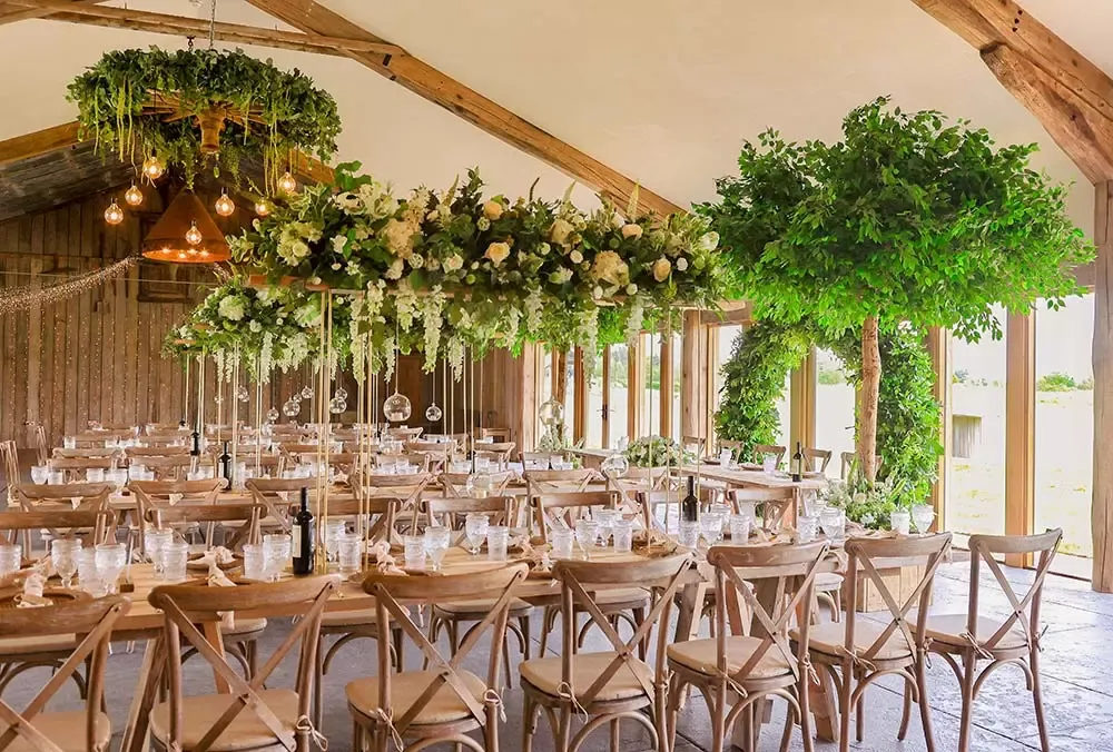 Stylish indoor reception space featuring elegant wooden tables, lush floral chandeliers, and greenery accents throughout the venue.