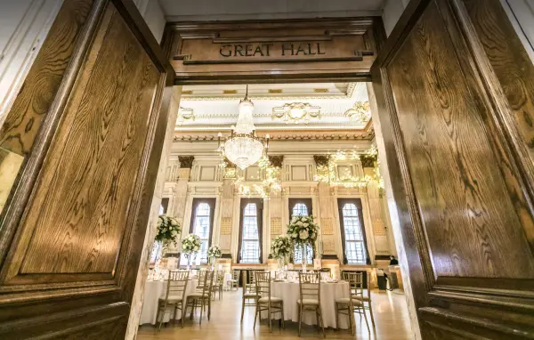 Elegant Great Hall entrance featuring chandeliers, tall windows, and beautifully arranged tables surrounded by greenery. Perfect for a timeless wedding.