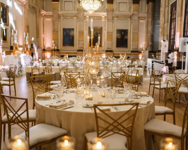 Elegant reception hall featuring round tables adorned with candles and chic chairs, set against grand architecture and soft lighting.
