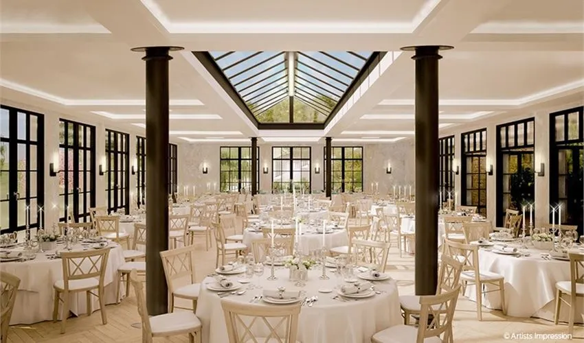Elegant banquet hall featuring tall windows, a glass roof, and white-clothed tables set for a wedding reception with natural light.