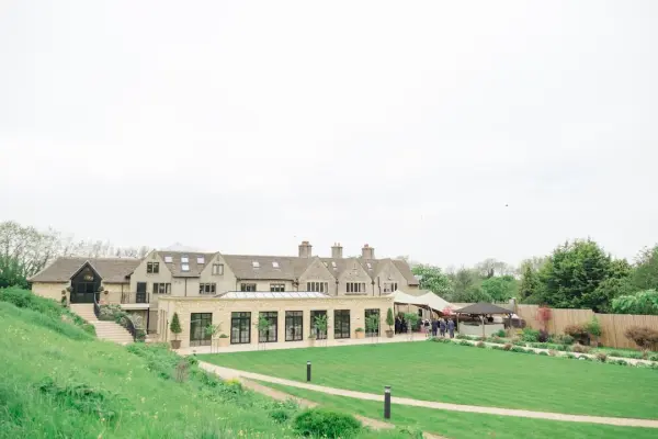 Charming countryside venue featuring a spacious lawn, elegant stone facade, and large windows, perfect for outdoor and indoor celebrations.