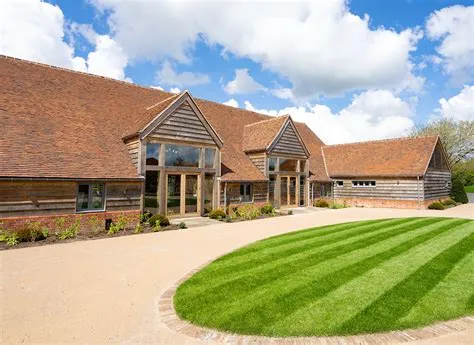 Charming rustic barn venue with large windows, lush green lawn, and well-maintained landscaping, perfect for a picturesque wedding.