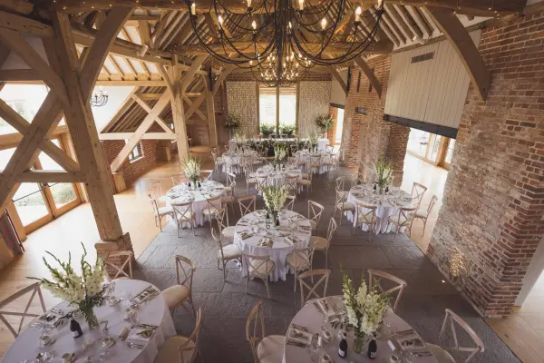 Rustic barn venue featuring charming wooden beams, elegant round tables with floral centerpieces, and large windows for natural light.