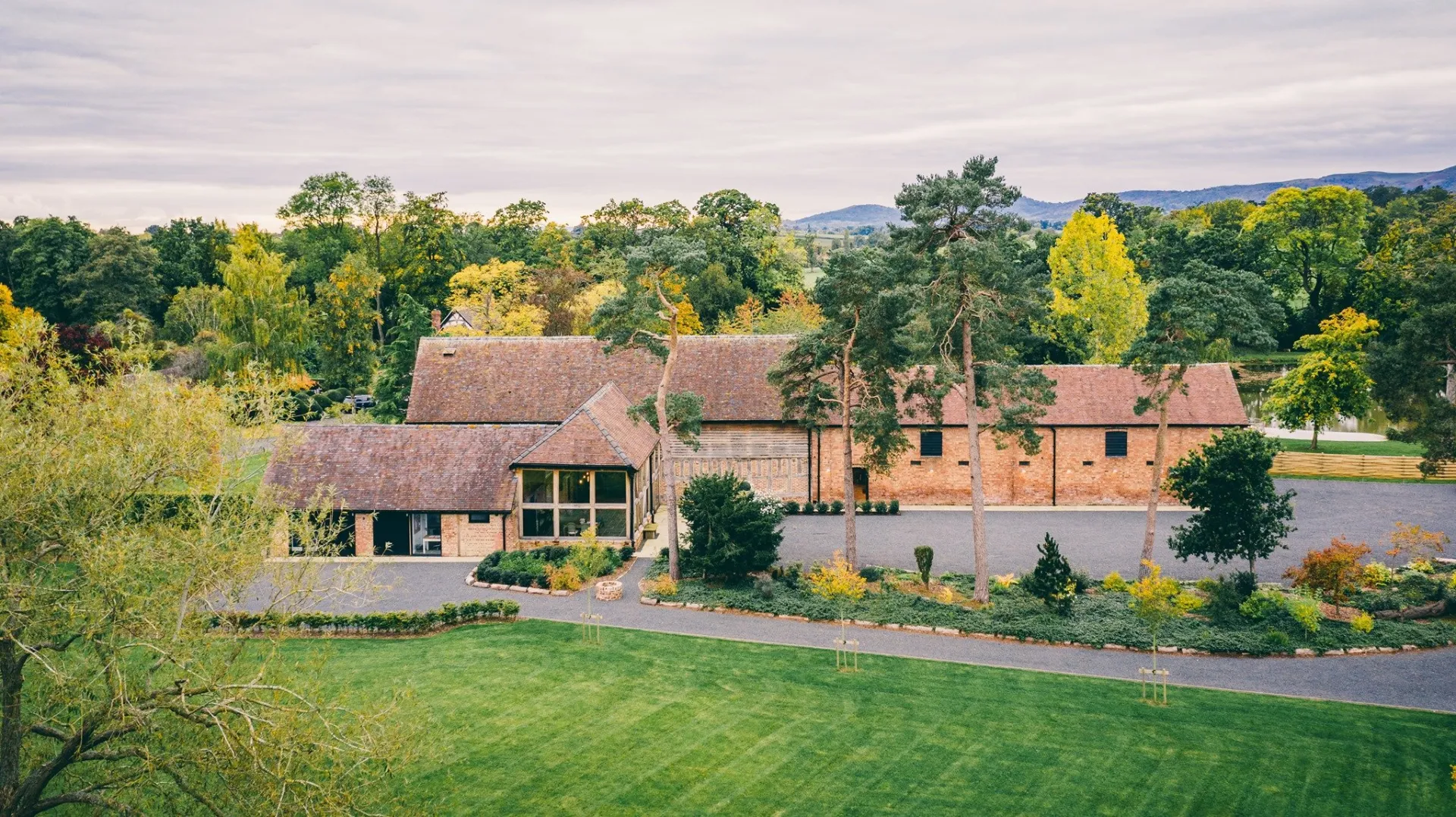 Charming rustic barn surrounded by lush greenery, featuring a spacious lawn and a picturesque setting perfect for outdoor weddings.