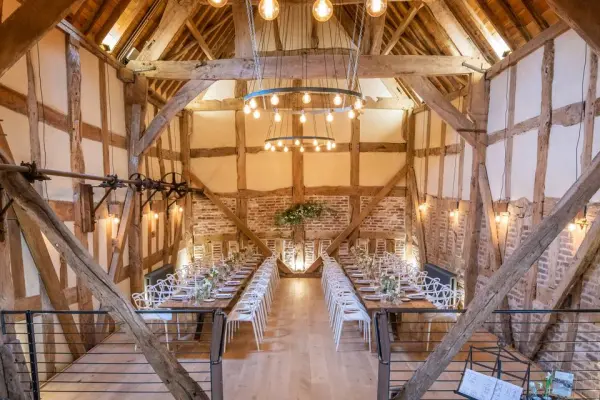 Stunning rustic barn interior featuring wooden beams and elegant lighting, set up for a wedding ceremony with rows of white chairs.
