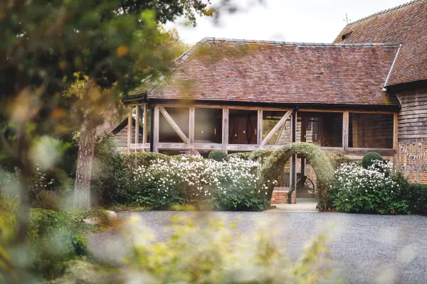 Charming rustic barn with a welcoming garden entrance, surrounded by lush greenery and blooming flowers, perfect for a romantic wedding.
