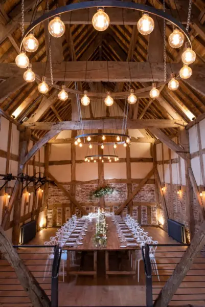 Rustic barn interior featuring a long wooden dining table, warm lighting, and exposed beams, perfect for an intimate wedding celebration.