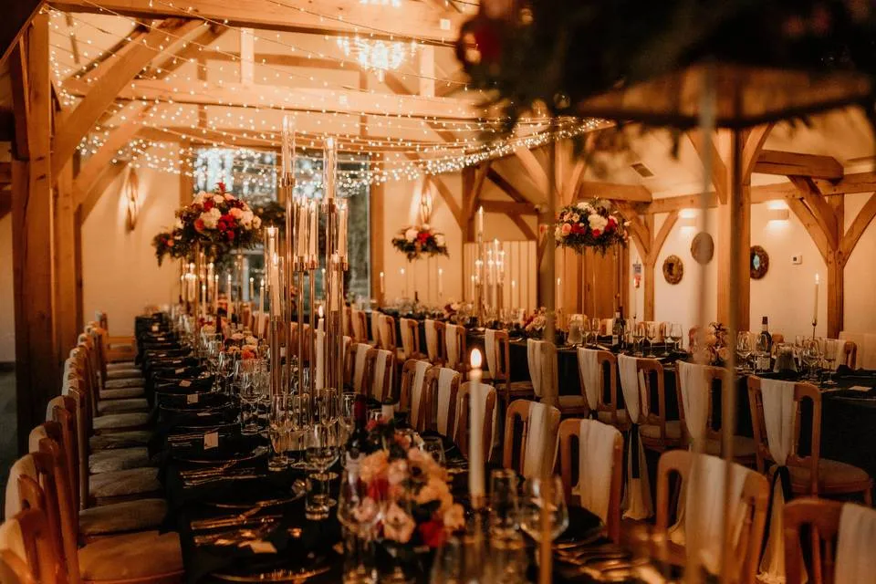 Elegant wooden beams frame a stunning reception space adorned with twinkling lights, floral centerpieces, and candlelit tables.