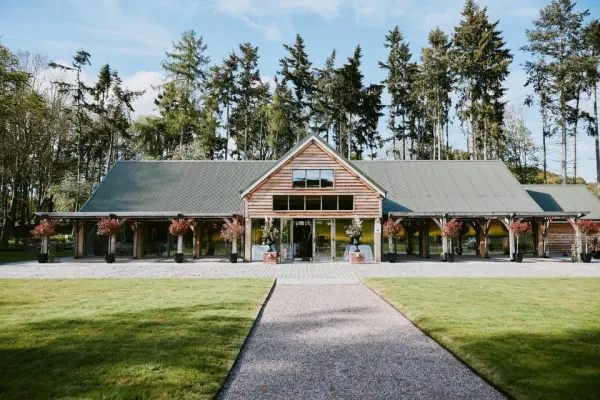 Charming rustic venue with a wooden facade, surrounded by lush trees and blooming planters, ideal for outdoor ceremonies and receptions.