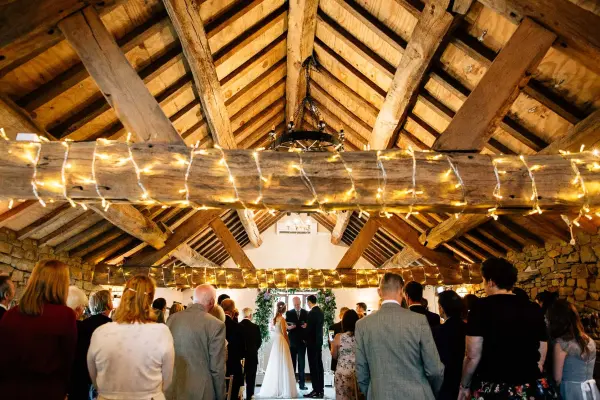 Charming barn interior with rustic wooden beams, warm string lights, and an intimate ceremony setting for couples and guests.