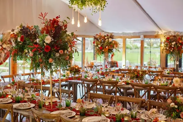 Elegant reception setting with floral centerpieces, rustic wooden tables, and warm lighting under a stylish tent. Perfect for intimate weddings.