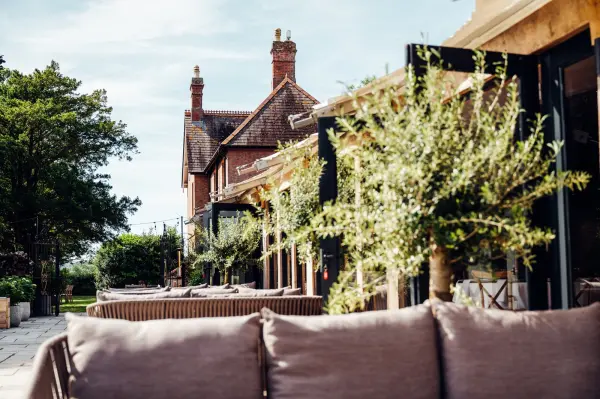 Charming outdoor lounge with modern seating, lush greenery, and a picturesque backdrop of a classic venue perfect for wedding celebrations.