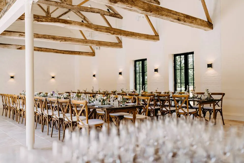 Rustic-chic reception area featuring wooden beams, elegant tables set for guests, and large windows inviting natural light.