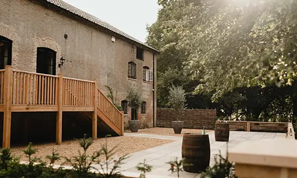 Rustic venue featuring a charming outdoor space with wooden decking, barrels, and lush greenery, perfect for a laid-back wedding celebration.