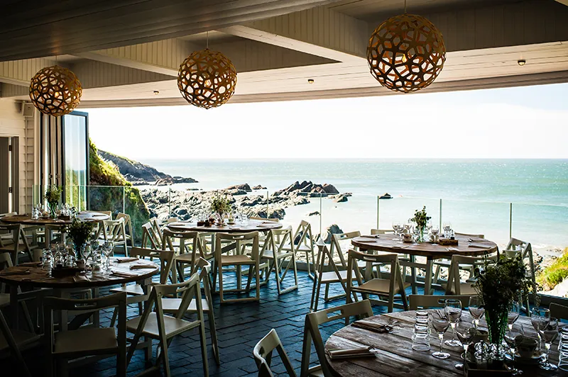 Coastal wedding venue featuring rustic tables, stylish decor, and sweeping ocean views through expansive windows.