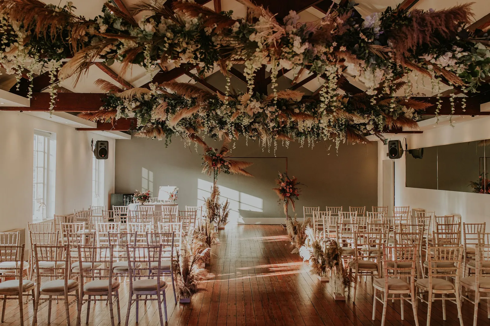 Charming indoor ceremony space with elegant wooden beams, floral decorations, and rows of chiavari chairs, perfect for a romantic wedding.