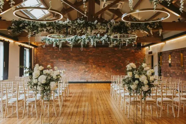 Rustic indoor wedding space features elegant floral arrangements, wooden floors, and stylish hanging lights, creating a warm and inviting atmosphere.
