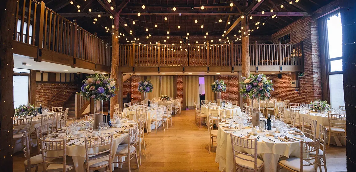 Rustic barn venue featuring elegant wooden beams, twinkling string lights, and beautifully set tables adorned with floral centerpieces.