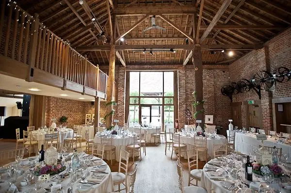 Rustic wedding venue featuring elegant round tables, exposed brick walls, and high wooden beams under abundant natural light.