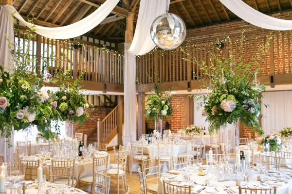 Charming rustic barn with elegant tables, lush floral arrangements, and draped fabric, featuring a sparkling disco ball overhead.