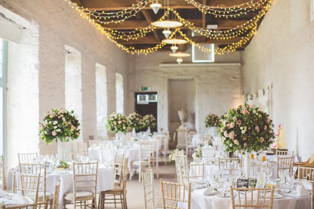 Elegant reception hall with wooden beams, twinkling fairy lights, and elegant floral centerpieces at each table, creating a romantic ambiance.
