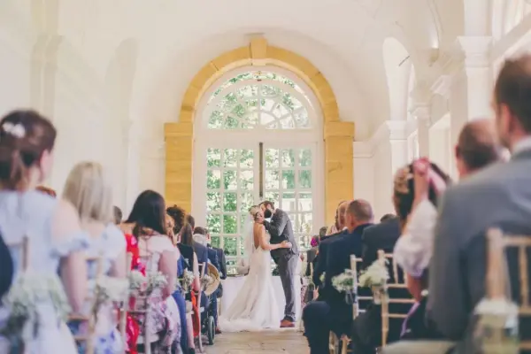Bright indoor ceremony space featuring a couple exchanging vows, surrounded by guests in elegant attire and beautiful natural light.