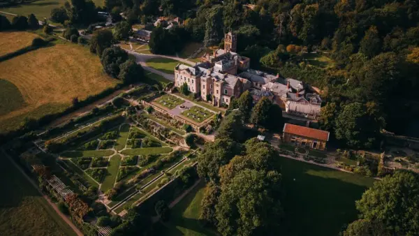 Aerial view of a stunning historic estate with lush gardens, manicured lawns, and a charming outdoor ceremony space surrounded by greenery.